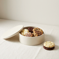 Open keepsake tin of assorted cookies with cookies stacked beside